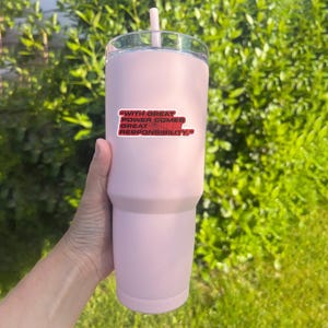 May include: A light pink tumbler with a clear lid and a pink straw. A red and white sticker on the tumbler reads "WITH GREAT POWER COMES GREAT RESPONSIBILITY."
