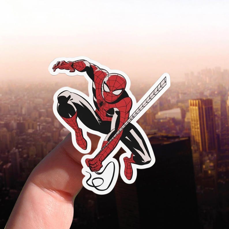 May include: A sticker depicting Spider-Man in a crouching pose, wearing his classic red and black suit. The sticker shows Spider-Man with his web-shooter and web. The background is a blurred cityscape.