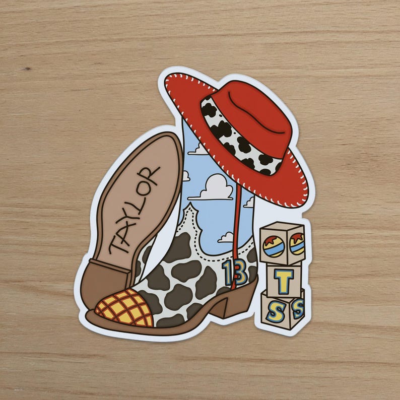 Puede incluir: Una pegatina que muestra una bota de vaquero con estampado de manchas de vaca, un fondo de cielo azul con nubes y un sombrero de vaquero rojo. La suela dice TAYLOR, el n&uacute;mero 13 est&aacute; en el lateral y hay una pila de tres cubos con las letras T y S.