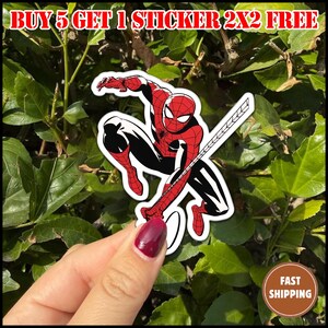 May include: A Spider-Man sticker in a dynamic pose, with a red and black costume and a white border. The sticker has the text "BUY 5 GET 1 STICKER 2X2 FREE" at the top. The background is green foliage.