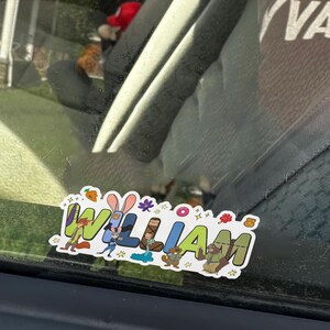 May include: A rectangular sticker featuring the name WILLIAM in large, colorful, block-style letters. Each letter incorporates various cartoon animal characters and small icons like a carrot, a donut, and a lollipop, all set against a white background.