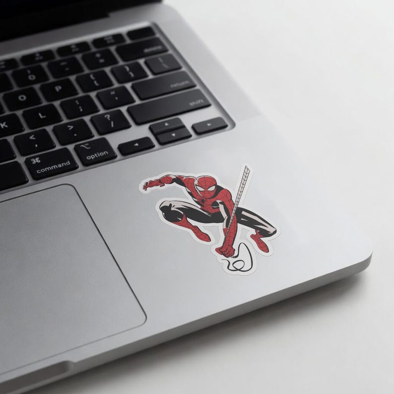 May include: A sticker of Spider-Man in a crouching pose, with red and black suit, holding a web. The sticker is on a silver laptop surface.