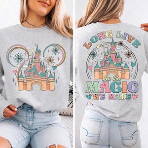Puede incluir: Sudadera gris claro con un diseño de castillo colorido y el texto "Long Live All The Magic We Made". El diseño frontal incluye un castillo, fuegos artificiales y orejas de Mickey Mouse.