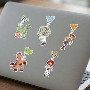 May include: A collection of colorful stickers featuring characters from the Toy Story movie franchise. The stickers include Rex the dinosaur, Buzz Lightyear, Woody, Jessie, and Bullseye, each holding a balloon.