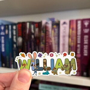 May include: A die-cut sticker featuring the name WILLIAM in colorful block letters, decorated with Zootopia-themed illustrations including Judy Hopps, Nick Wilde, Flash the sloth, a carrot, a donut, a paw print, and a police badge icon.