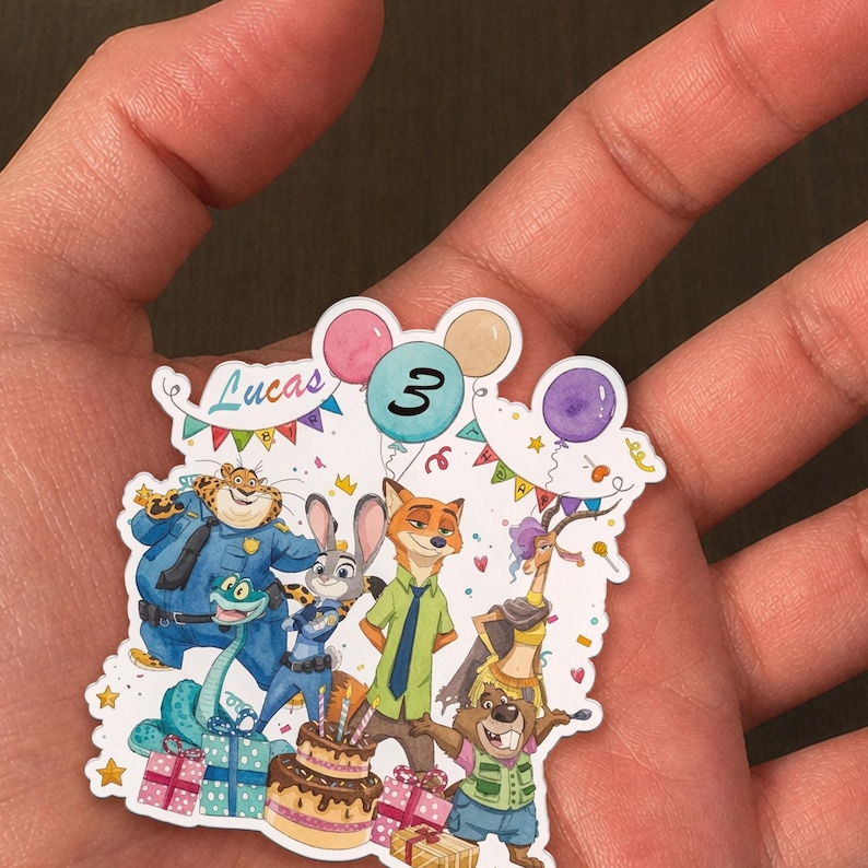 May include: A die-cut sticker featuring Zootopia characters including Judy Hopps, Nick Wilde, Chief Bogo, and Gazelle. The design includes a birthday cake, colourful balloons, confetti, and the text Lucas and the number 3 in a balloon.