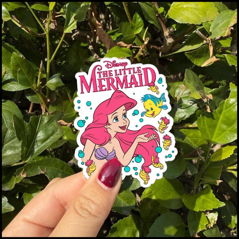 Op de afbeelding: Een gestanste sticker met het Disney The Little Mermaid logo in roze tekst bovenaan. De illustratie toont Ari&euml;l met lang roze haar, een paarse schelpentop en een blauwe Botje-vis, omringd door kleine zeepaardjes en blauwe bubbels.