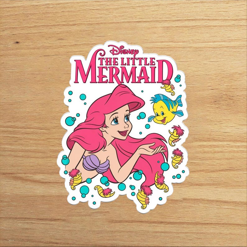 Op de afbeelding: Een gestanste sticker met Ariel uit Disney's De Kleine Zeemeermin met felroze haar, een paarse schelpentop en de gele vis Botje. Het ontwerp bevat verschillende kleine gele zeepaardjes en turquoise bubbels, met de tekst Disney THE LITTLE MERMAID in het roze bovenaan gedrukt.