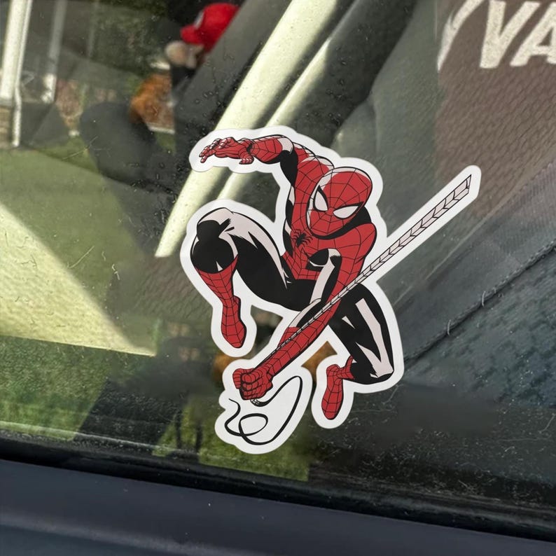 May include: A sticker of Spider-Man in a dynamic pose, with a red and black costume. The sticker has a white border and depicts the superhero with his web-shooters and web.