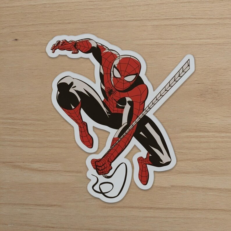 May include: A sticker of Spider-Man in a crouching pose, with his red and black suit and web-slinging design. The sticker has a white border and is set against a light wood-grain background.