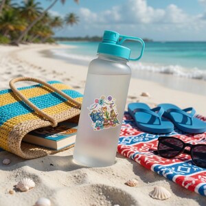 May include: A frosted clear plastic water bottle with a teal cap and a sticker featuring cartoon characters, balloons, and the number 3. The bottle is positioned upright on a sandy surface, showcasing a functional design with a carry handle.