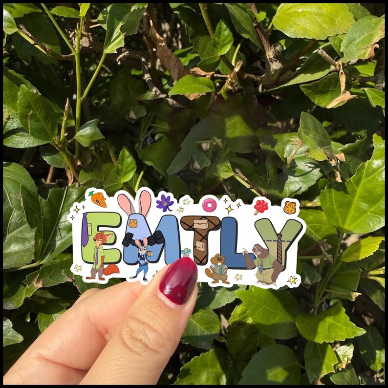 May include: A die-cut sticker featuring the name EMILY spelled out with cartoon characters and icons. The letters are decorated with Zootopia-themed elements including a fox, a rabbit, a sloth, and small items like a carrot, donut, and badge.