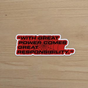 May include: A red sticker with the quote "WITH GREAT POWER COMES GREAT RESPONSIBILITY." The text is in black, with a spiderweb design in the center. The sticker has a white border.
