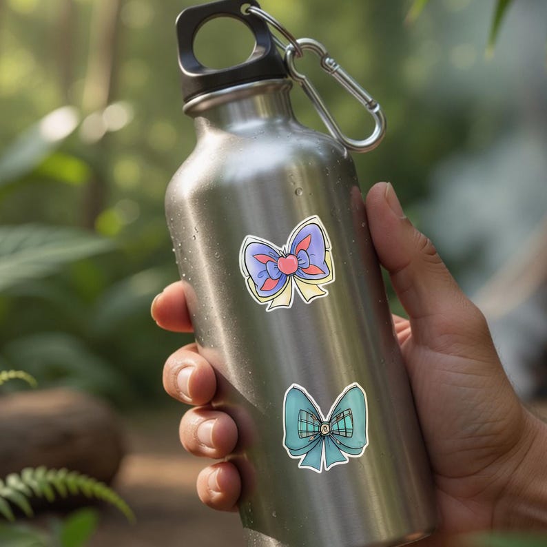 May include: Two stickers of bows are affixed to a stainless steel water bottle. The top bow is purple, red, and yellow. The bottom bow is teal with a plaid center. The bottle has a black cap and a silver carabiner.