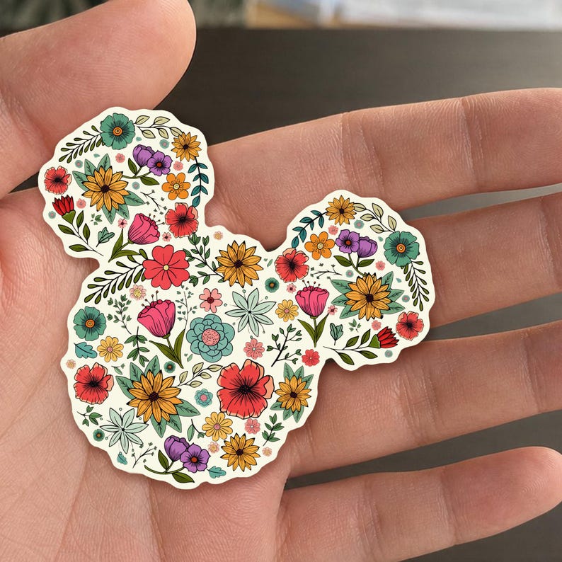 May include: A floral sticker in the shape of a mouse head. The sticker is filled with colorful flowers in shades of red, pink, yellow, purple, and blue, with green leaves. The background is off-white.