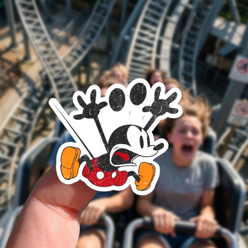 May include: A distressed sticker of Mickey Mouse in a state of panic, with arms raised and mouth agape. The sticker is held in front of a blurred background of a roller coaster and people screaming.