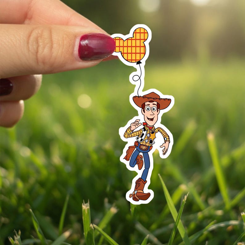 May include: A sticker of the character Woody from Toy Story, wearing a cowboy hat, vest, and blue jeans, running and holding a Mickey Mouse balloon. The balloon is yellow and red. The background is green grass.