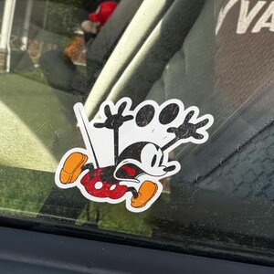 May include: A sticker featuring a distressed cartoon Mickey Mouse in a dynamic pose. Mickey is depicted in his classic colors: black, red, yellow, and white. The word "ZOOM" is above Mickey's head, with a distressed, vintage aesthetic.