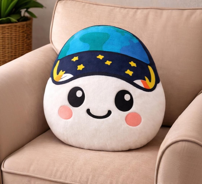 May include: A plush, egg-shaped pillow with a smiling face and a blue and navy blue design resembling a planet and starry night. The pillow has black eyes, pink cheeks, and a curved black mouth. It rests on a beige armchair.