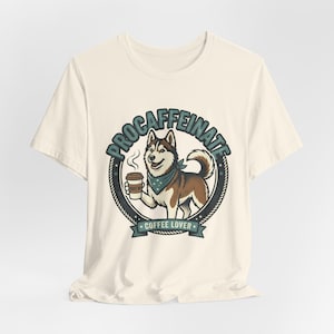 May include: Cream-colored t-shirt featuring a cartoon husky dog holding a coffee cup. The dog is wearing a blue bandana and is inside a circular design with the words "PROCAFFEINATE" and "COFFEE LOVER".