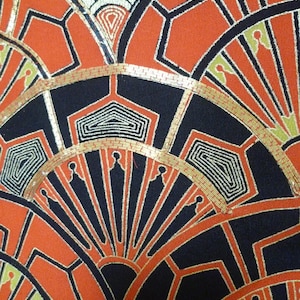 以下が含まれることがあります： アールデコデザインの生地のクローズアップ。オレンジ、黒、金色の扇形の要素と幾何学的なディテールが特徴です。生地は質感があり、高品質の素材を示唆しています。
