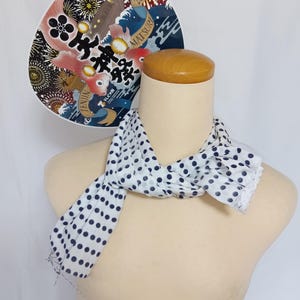 May include: A white scarf with navy blue polka dots and a lace trim is draped on a mannequin. Behind it is a decorative fan with Japanese text and illustrations of koi carp, waves, and fireworks.