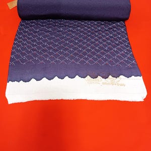 Puede incluir: Un textil azul marino enrollado con un patrón de diamantes de puntos blancos y acentos rojos. El borde inferior tiene un borde blanco festoneado. El textil está sobre una superficie roja. La etiqueta dice "A302ZT".