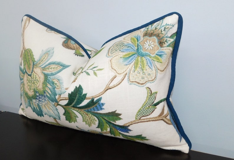 May include: A white pillow with a floral pattern in shades of green, blue, and brown. The pillow has a teal blue border.