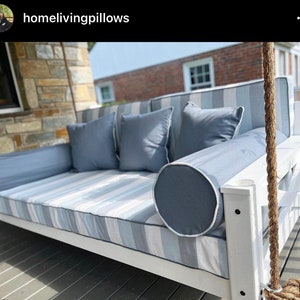 May include: White porch swing with blue and white striped cushions and blue throw pillows. The swing is hanging from a rope and is on a wooden deck.
