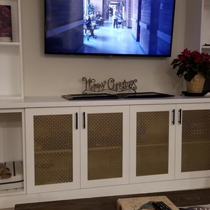 May include: White cabinet with two dog beds, each with a dog sleeping on it. The cabinet has four doors with a woven pattern and black handles. Above the cabinet is a flat screen TV and a white shelf with a red poinsettia plant.