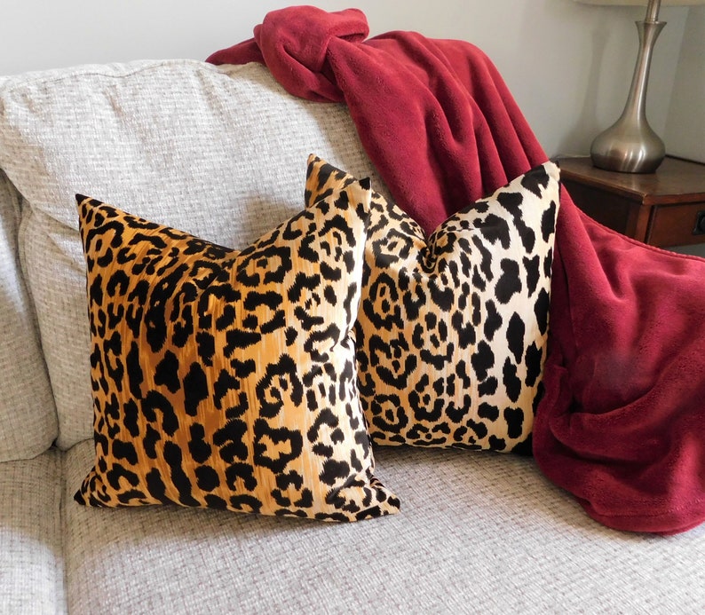 Pu&ograve; includere: Due cuscini da divano con stampa leopardata su un divano bianco con una coperta rossa drappeggiata sullo schienale del divano.