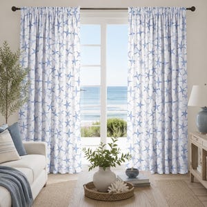 Puede incluir: Un par de cortinas de cuerpo entero con un patrón repetitivo de estrellas de mar azules sobre un fondo blanco. Las cortinas cuelgan de una barra oscura y están colocadas frente a una ventana grande con vistas a la costa y al océano.