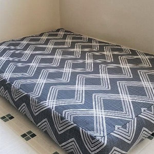 May include: A gray and white chevron patterned dog bed. The bed is rectangular and has a thick, padded cushion.