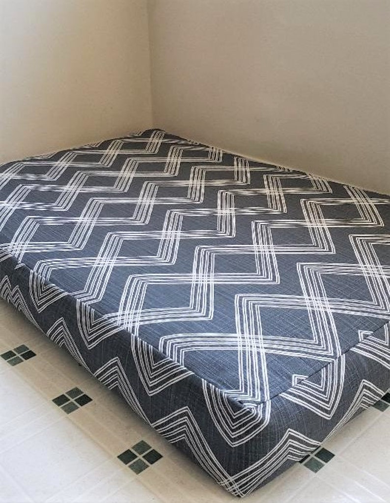 May include: A gray and white chevron patterned dog bed. The bed is rectangular and has a thick, padded cushion.