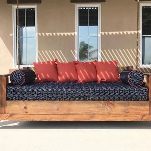 May include: A wooden swing bed with a black and white patterned mattress and red throw pillows. The swing bed is hanging from the ceiling with ropes.