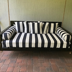 May include: A black wooden swing bed with a white and black striped cushion and pillows. The swing bed is hanging from a porch ceiling.