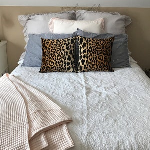 Pu&ograve; includere: Un letto bianco con un piumino bianco e due cuscini con stampa leopardata. Una coperta in spugna a nido d'ape rosa &egrave; piegata ai piedi del letto.