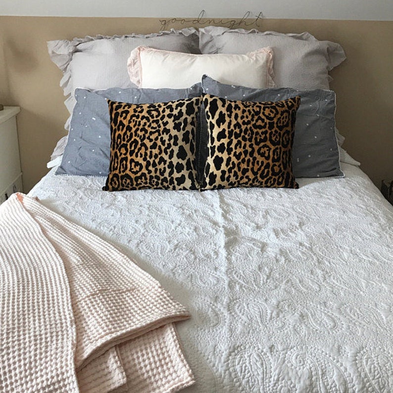 Pu&ograve; includere: Un letto bianco con un piumino bianco e due cuscini con stampa leopardata. Una coperta in spugna a nido d'ape rosa &egrave; piegata ai piedi del letto.