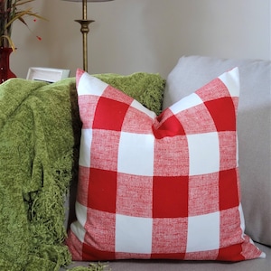 May include: Red and white buffalo check cushion with a green throw on a sofa.