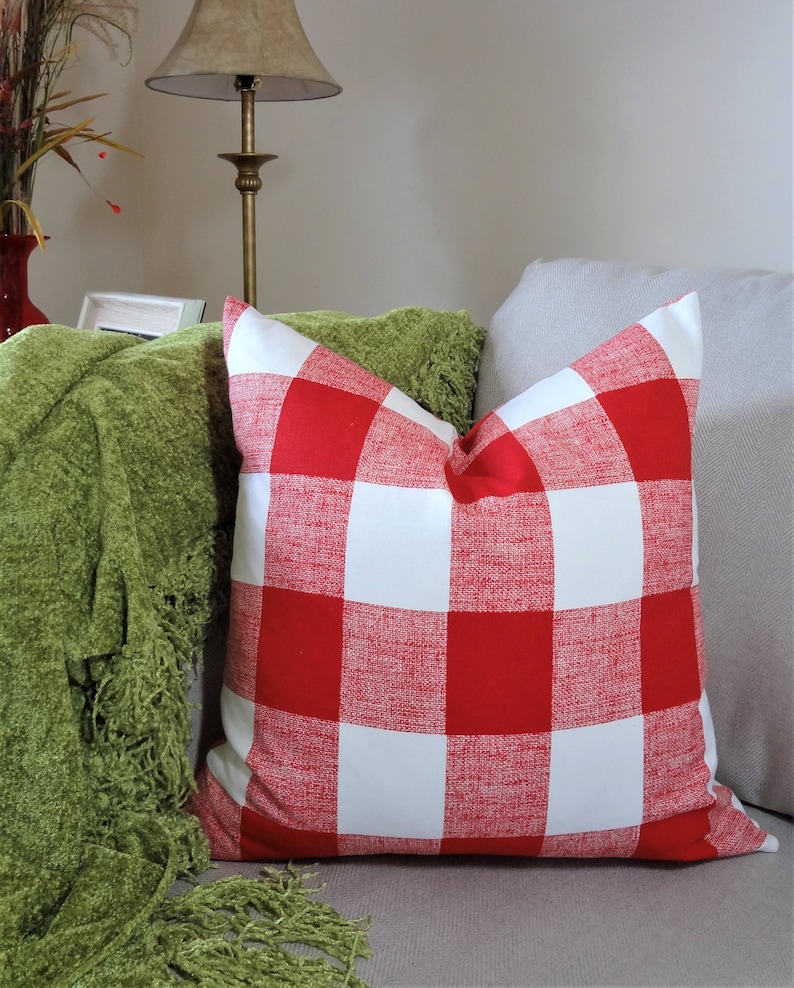 May include: Red and white buffalo check cushion with a green throw on a sofa.
