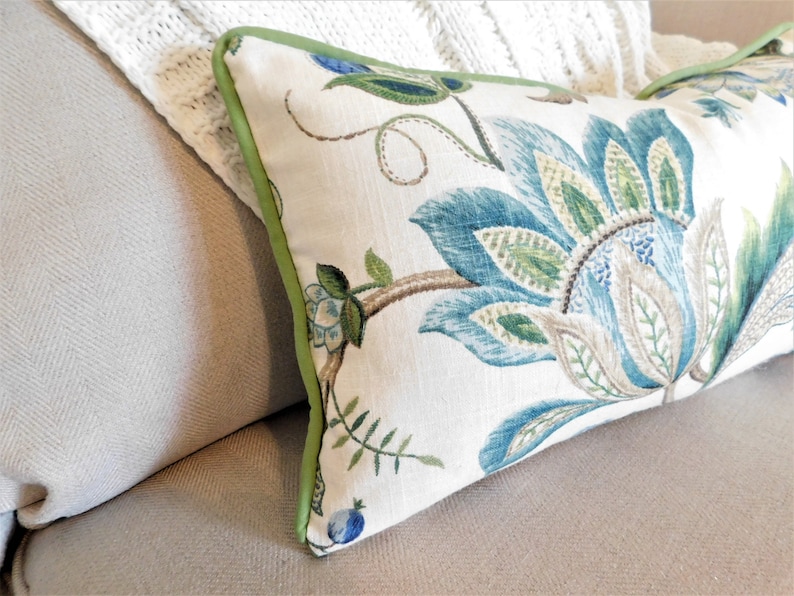 May include: A decorative throw pillow with a floral design featuring blue, green, and brown colors. The pillow has a green border and is made of a soft, textured fabric.