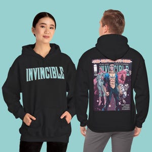 May include: Black hoodie featuring the word "INVINCIBLE" in light blue on the front. The back displays a comic book cover with the title "THE VILTRUMITE WAR" and superhero illustrations.