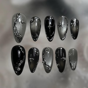 May include: Set of ten almond-shaped false nails in shades of black and gray. Some nails feature silver embellishments, including lines and small, round studs. The nails have a glossy finish, creating a modern and edgy aesthetic.