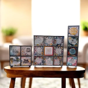 May include: Three decorative framed art pieces with inspirational quotes and floral designs. The pieces are in black metal frames and sit on a wooden table. The quotes include "Just Breathe", "Think Positive", and "Be the Light".