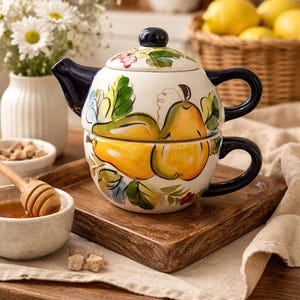 Può includere: Servizio da tè in ceramica dipinto a mano con disegni di pere gialle e foglie verdi. La teiera ha un manico e un coperchio blu navy. Il set è su un vassoio di legno, con una ciotola di miele e un cesto di limoni sullo sfondo.