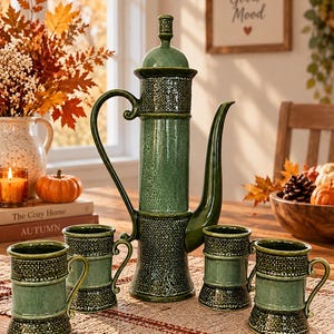 May include: A tall, cylindrical green ceramic coffee pot with a lid, a curved handle, and a long spout, accompanied by four matching mugs. Each piece features a textured, woven-like pattern on the top and bottom sections with a smooth centre.