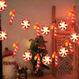 Pode incluir: Uma guirlanda de luzes de Natal com luzes em forma de bengala doce e enfeites. As bengalas doces são vermelhas e brancas, e os enfeites têm um design de estrela. Ideal para decorações de férias.