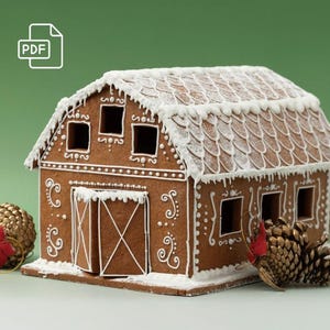 Op de afbeelding: Een peperkoeken schuur met witte glazuurdetails en een met sneeuw bedekt dak. De bruine structuur heeft ramen en een schuurdeur. Decoratief gouden ornament en dennenappel met rood lint aan de zijkant. Feestelijke vakantiedecoratie.