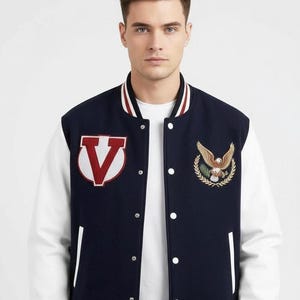 May include: Navy blue and white varsity jacket with a red and white letter "V" patch and an embroidered eagle emblem. The jacket has a button-up front and striped detailing on the collar and cuffs.