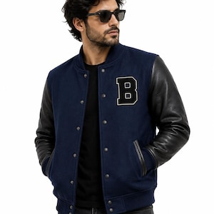 May include: Navy blue varsity jacket with black leather sleeves. The jacket features a large black and white letter "B" patch on the chest. It has a button-up front and pockets. A classic style.